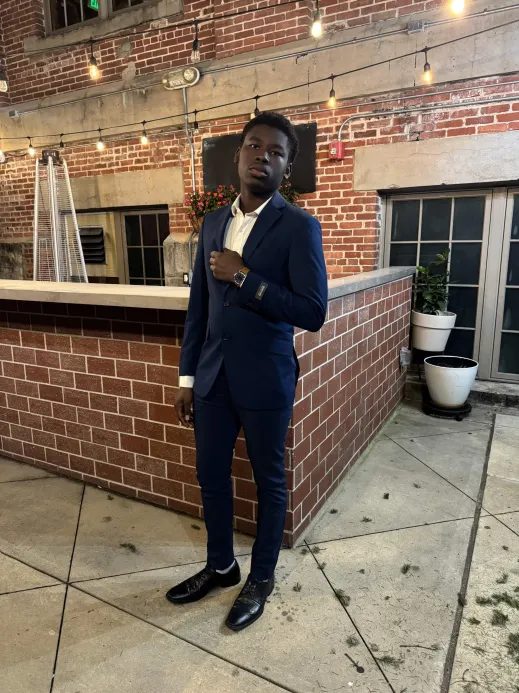 Joshua in a navy suit near a brick wall