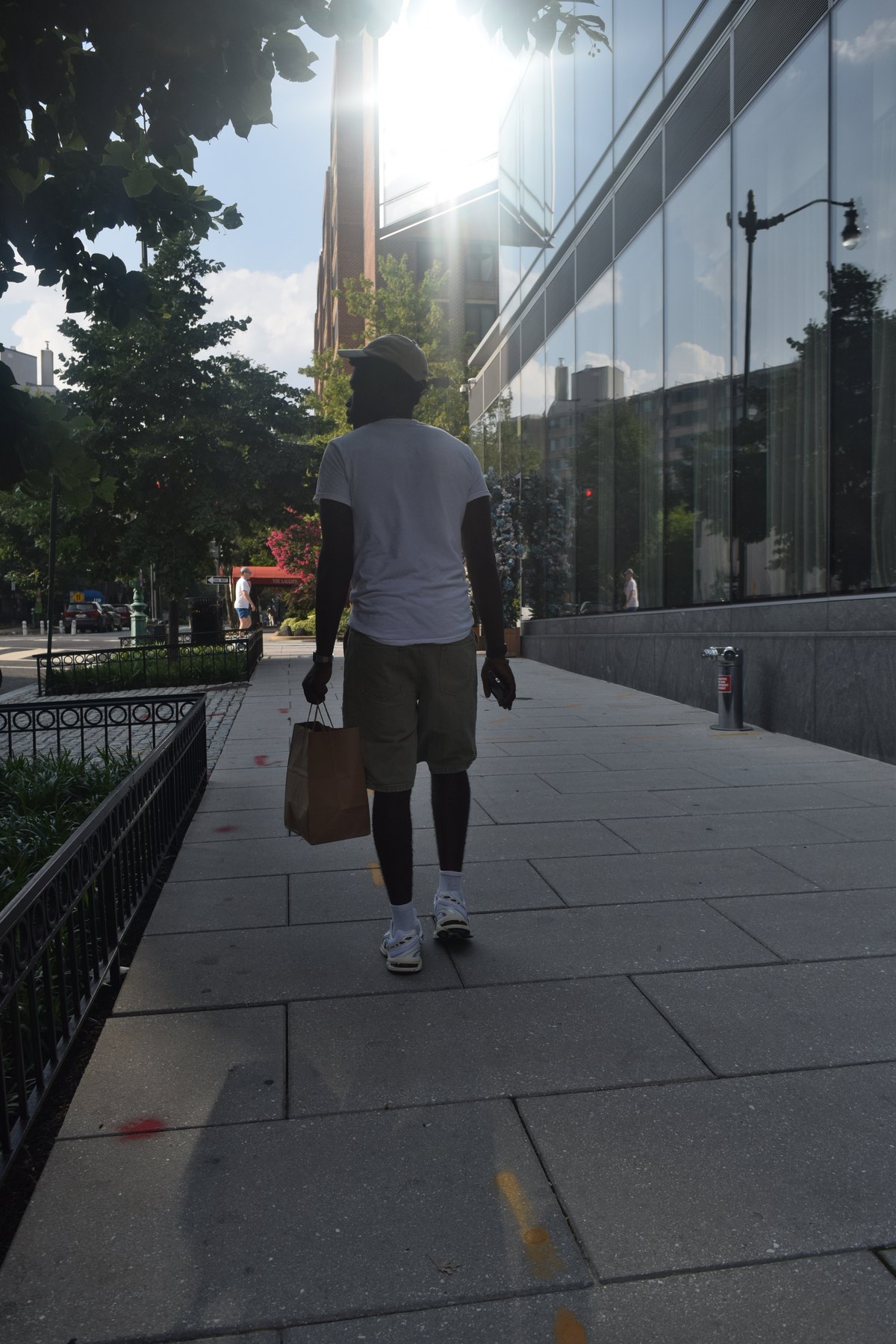 Joshua walking down a DC sidewalk in backlight with a shopping bag
